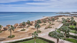 Ein Strandresort mit Palmen, Reetdachschirmen und freiem Blick auf das Meer.