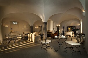 A spacious room with high ceilings and arched structures, featuring a fireplace, seating area, and a dining table.