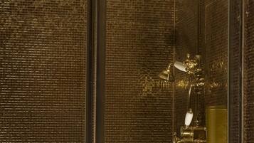 A shower with a textured wall and a gold-colored showerhead.