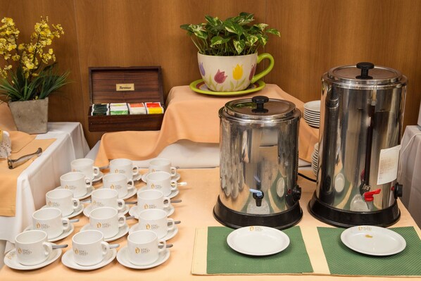 Una mesa de desayuno con varias cafeteras, teteras y una variedad de tazas y platillos.