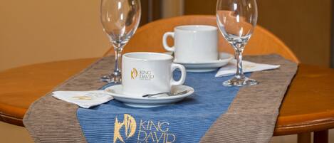 A dining table with two white cups and two wine glasses, a napkin, and a placemat with the King David logo.