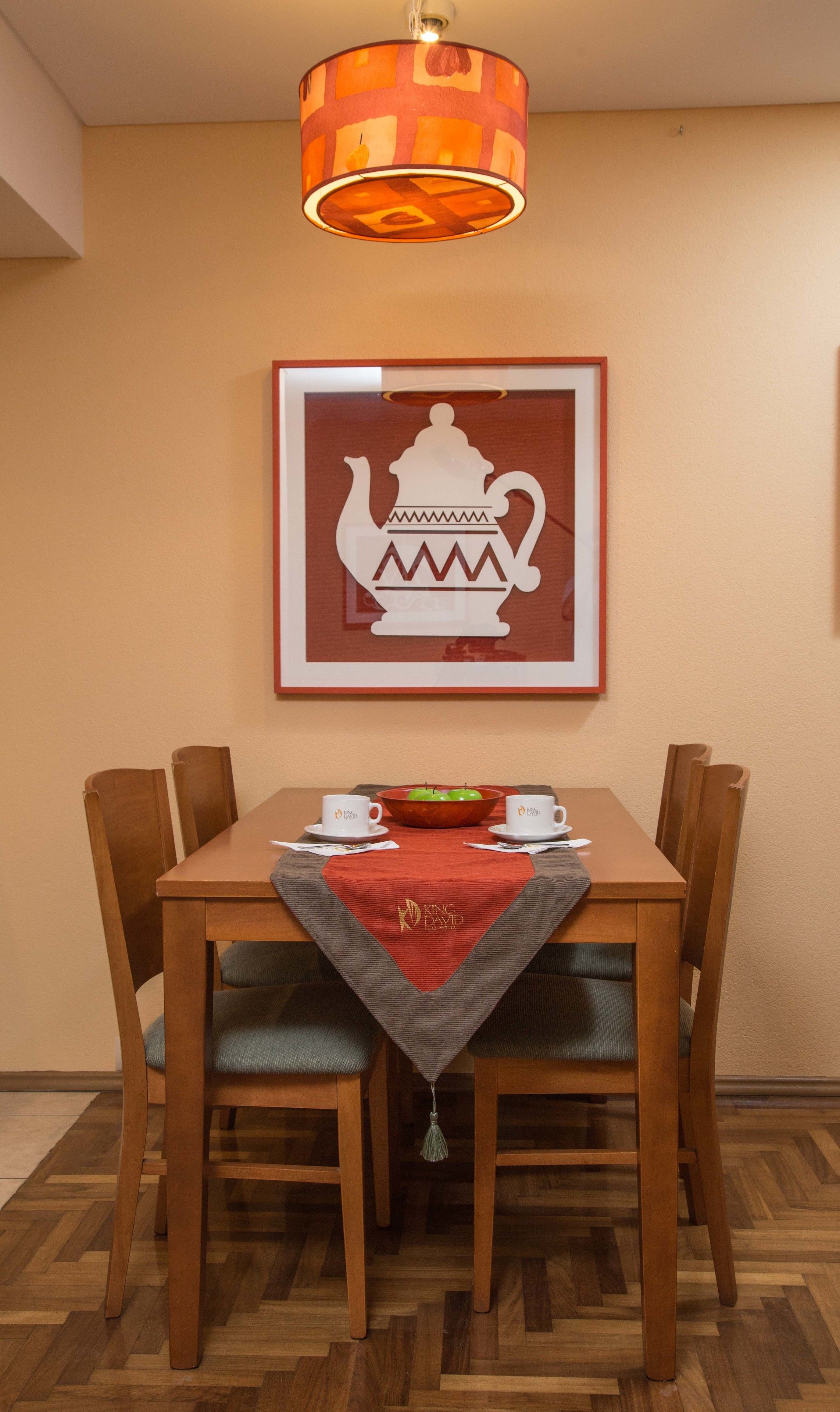 A dining area with a wooden table, four chairs, a framed teapot artwork, and a hanging lamp.