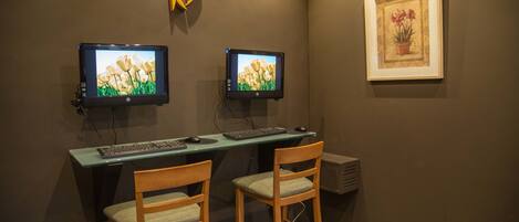 A workspace with two monitors, a keyboard, and two wooden chairs.