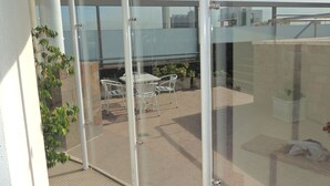 Un balcón acristalado con una mesa y sillas, plantas en macetas y vistas de la ciudad.