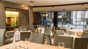Un restaurante con varias mesas dispuestas para comer, con un interior moderno que incluye divisiones de vidrio y vistas a la calle.