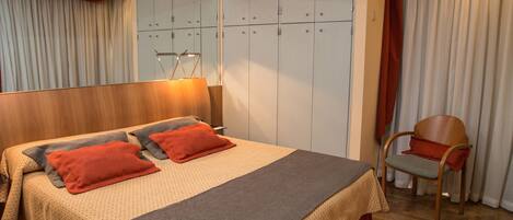 A hotel room with a large bed, a wooden headboard, a chair, and a wardrobe with multiple doors.