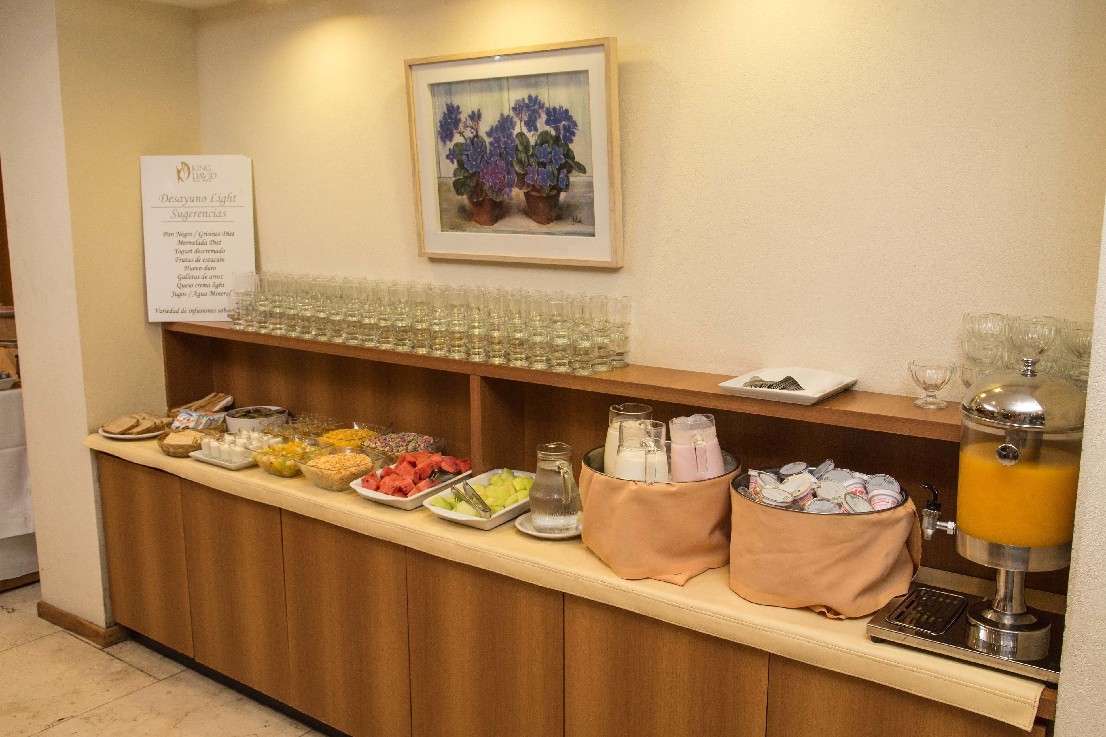 Un comptoir de buffet proposant divers plats, un distributeur de jus de fruits et un tableau encadré accroché au mur.