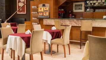 Un restaurante con mesas dispuestas para comer, una zona de bar con botellas y una escalera.