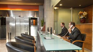 Una zona de recepción moderna con un mostrador largo, sillas de cuero negro, un refrigerador de acero inoxidable y una planta en maceta.