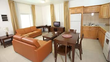 Ein Wohnzimmer mit Sofa, einem Esstisch mit Stühlen, einem Fernseher und einer Küchenzeile inklusive Schränken und Geräten.