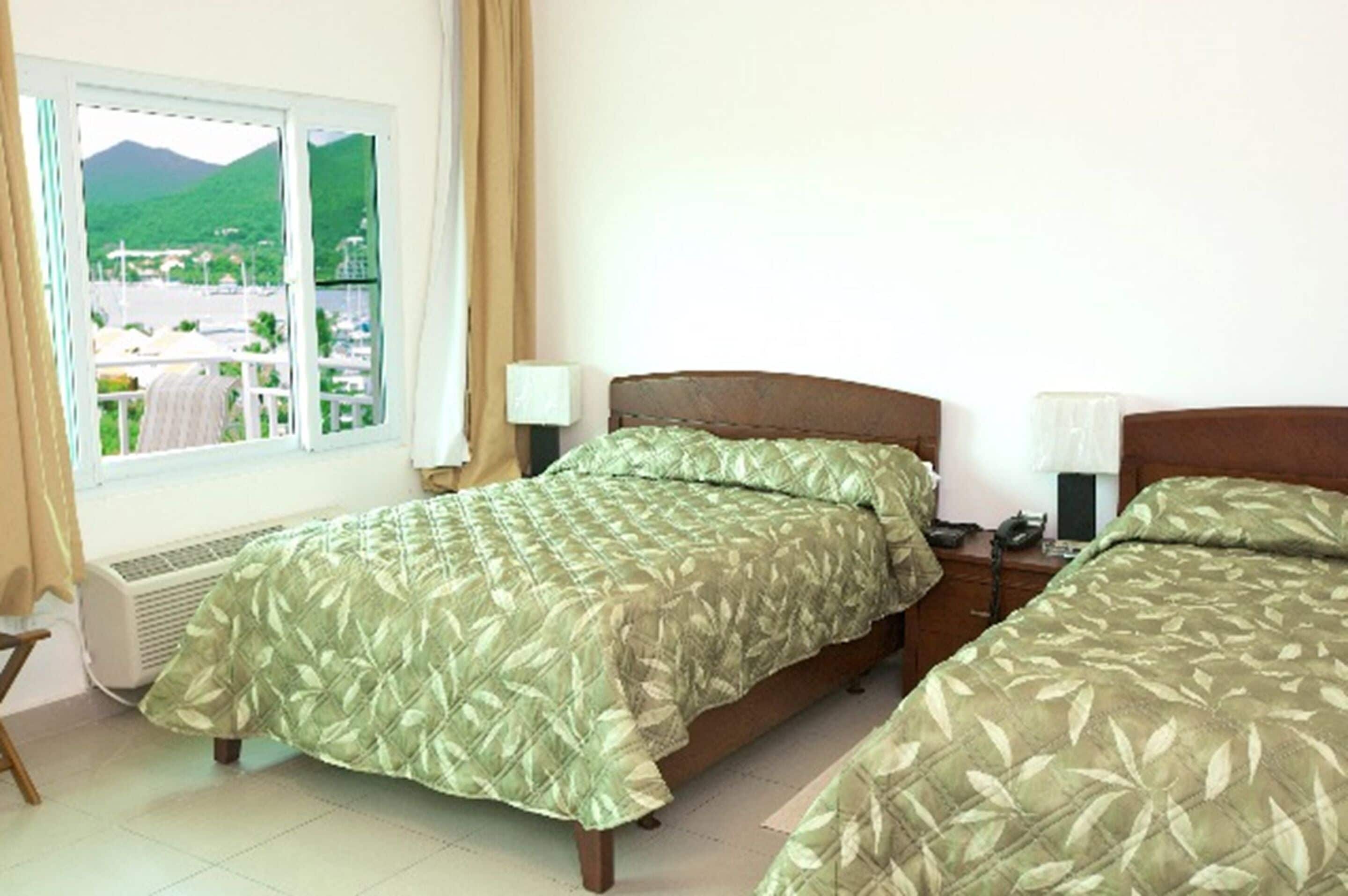 A hotel room with two beds, a window with a view of a mountain and a city, and a desk with a lamp.