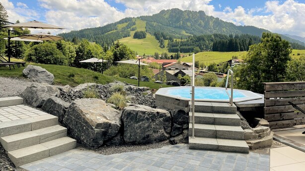A pool area with stone steps and a view of a mountainous landscape. - Berghotel Tirol (Jungholz)