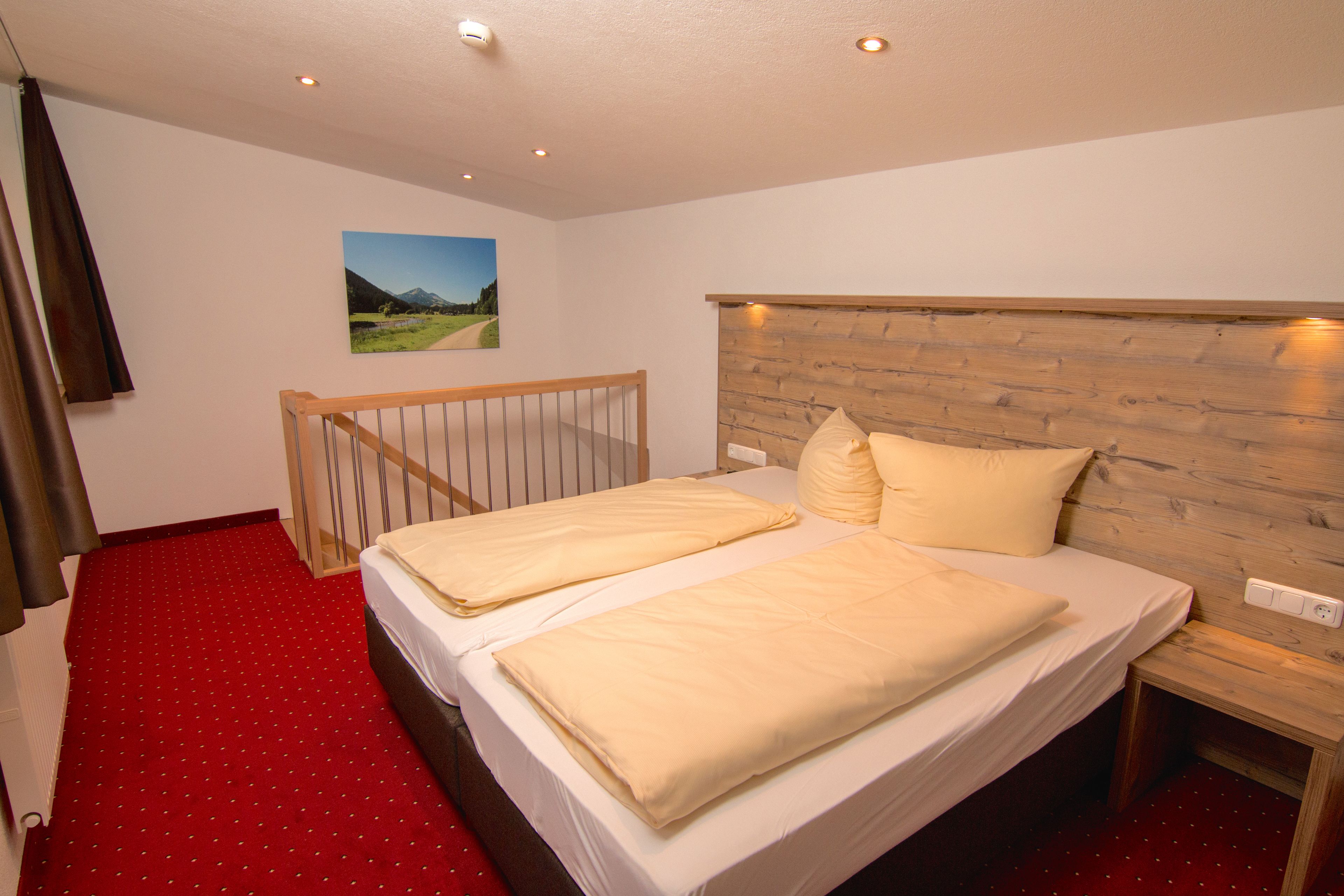 Ein Schlafzimmer mit einem Holzkopfteil, zwei Betten mit beige farbenen Bettwäsche, einem roten Teppich und einem Bild an der Wand.