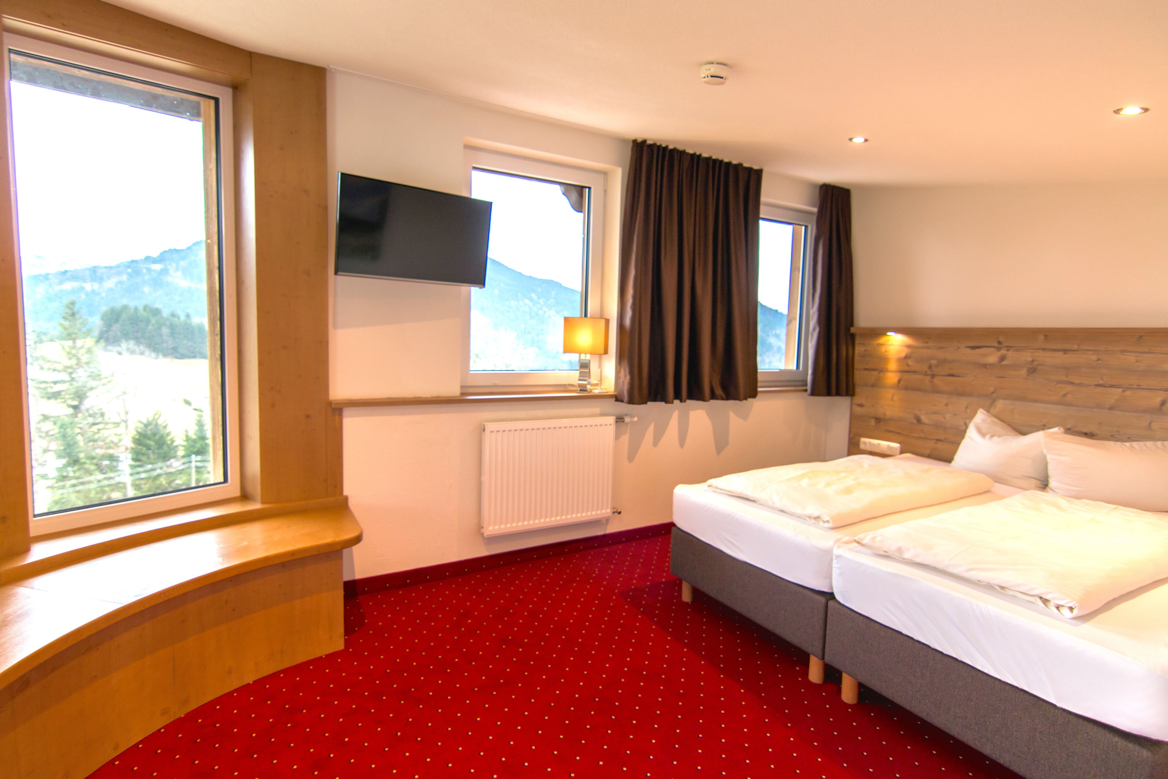 A hotel room with two beds, a TV mounted on the wall, a window with curtains, and a view of the mountains.