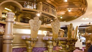 A bar area with ornate wooden furniture and a ceiling fan. - Berghotel Tirol (Jungholz)