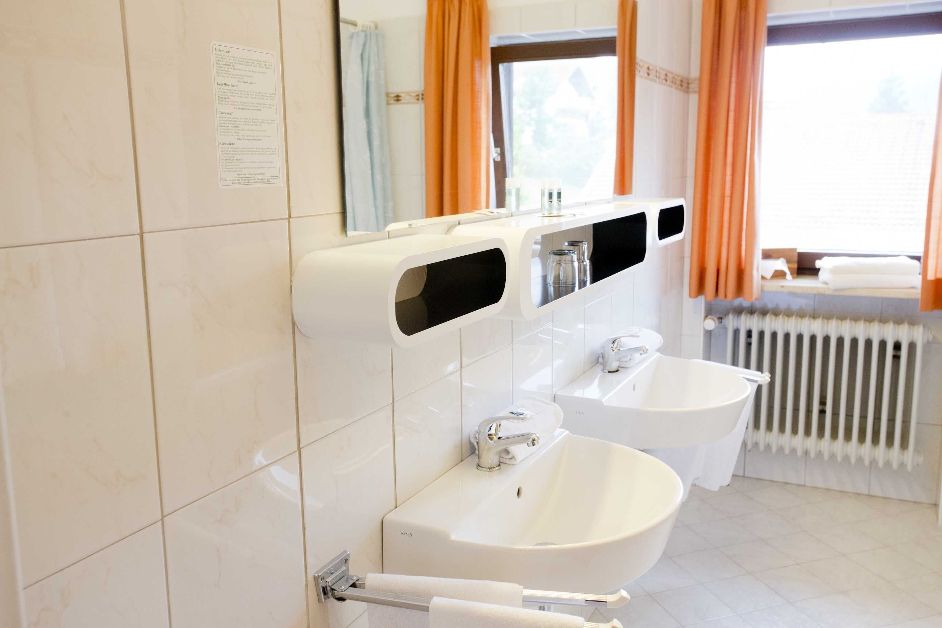 A modern bathroom with two sinks, a mirror, and a window with curtains.