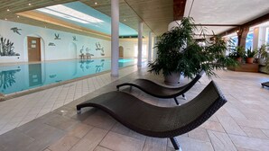 A spacious indoor pool area with a clear view of the pool, lounge chairs, and potted plants. - Berghotel Tirol (Jungholz)
