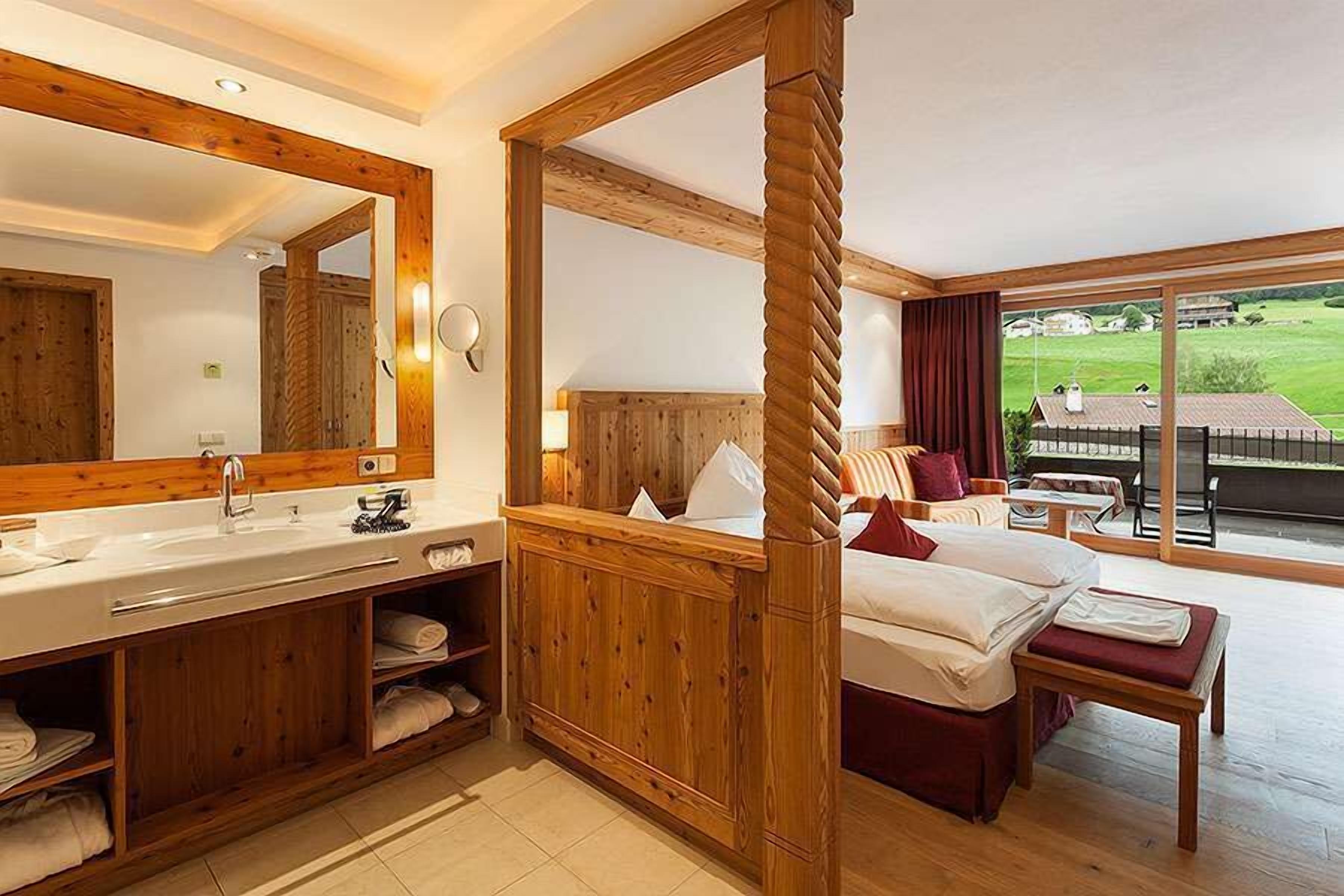 Camera d'albergo con arredamento in legno, un letto grande, un bagno con lavandino e specchio, e vista sull'esterno.