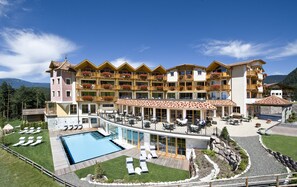 A multi-story hotel with a pool, outdoor seating, and mountain views.