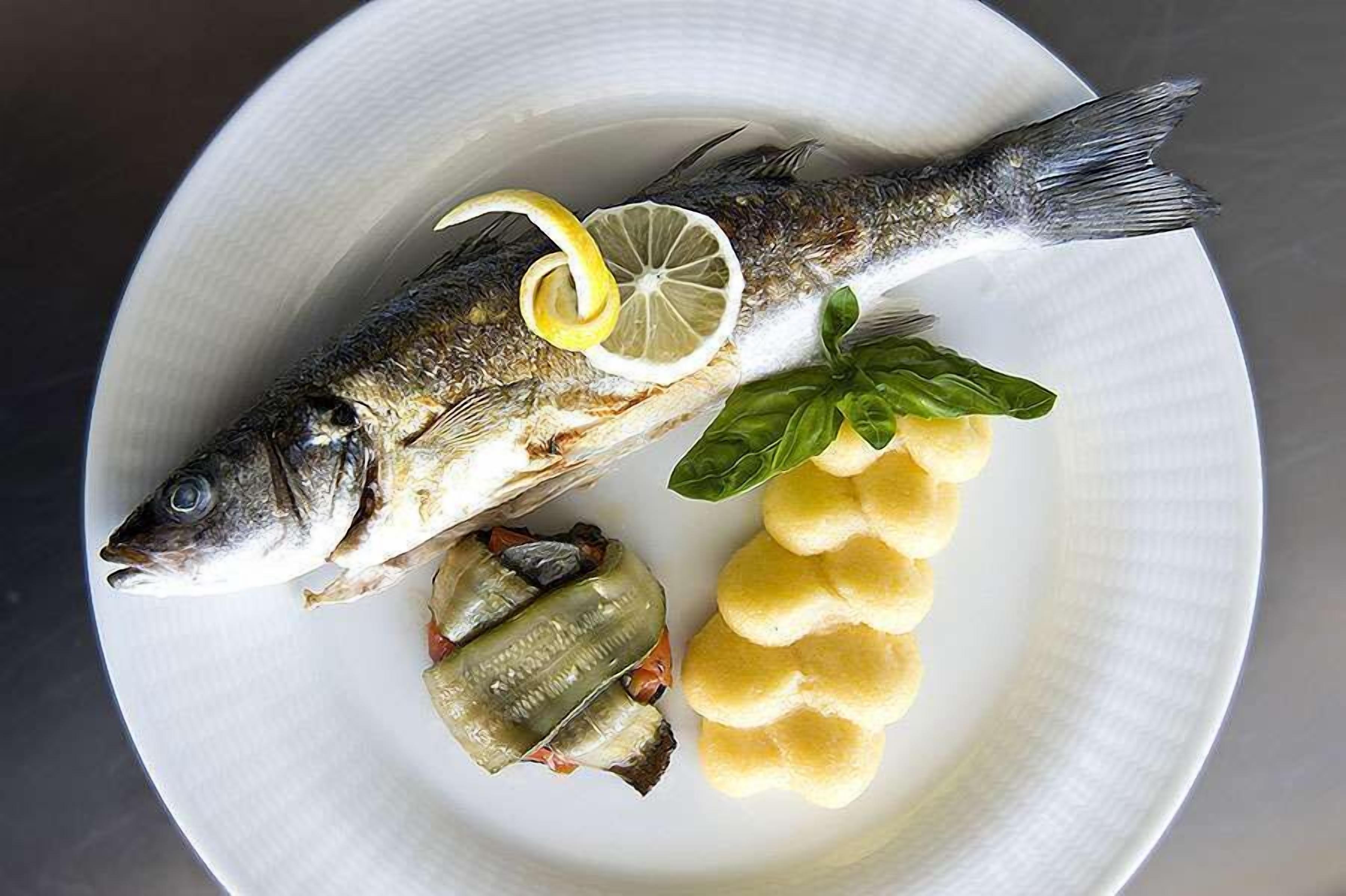 Un plato con un pescado entero, rodajas de limón y pimientos rellenos.