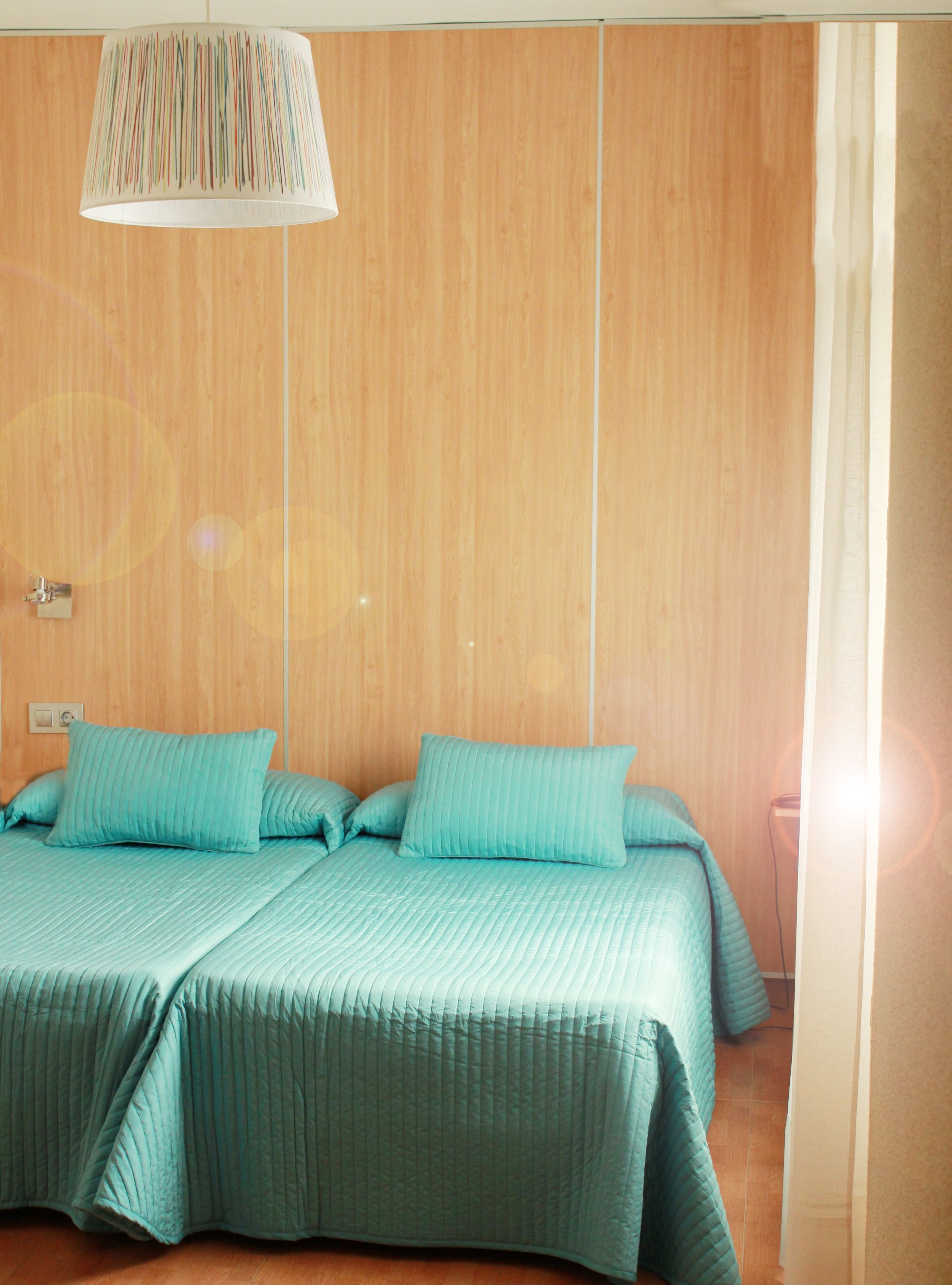 Una habitación con pared de paneles de madera, cama con ropa de cama color turquesa y una lámpara colgante.
