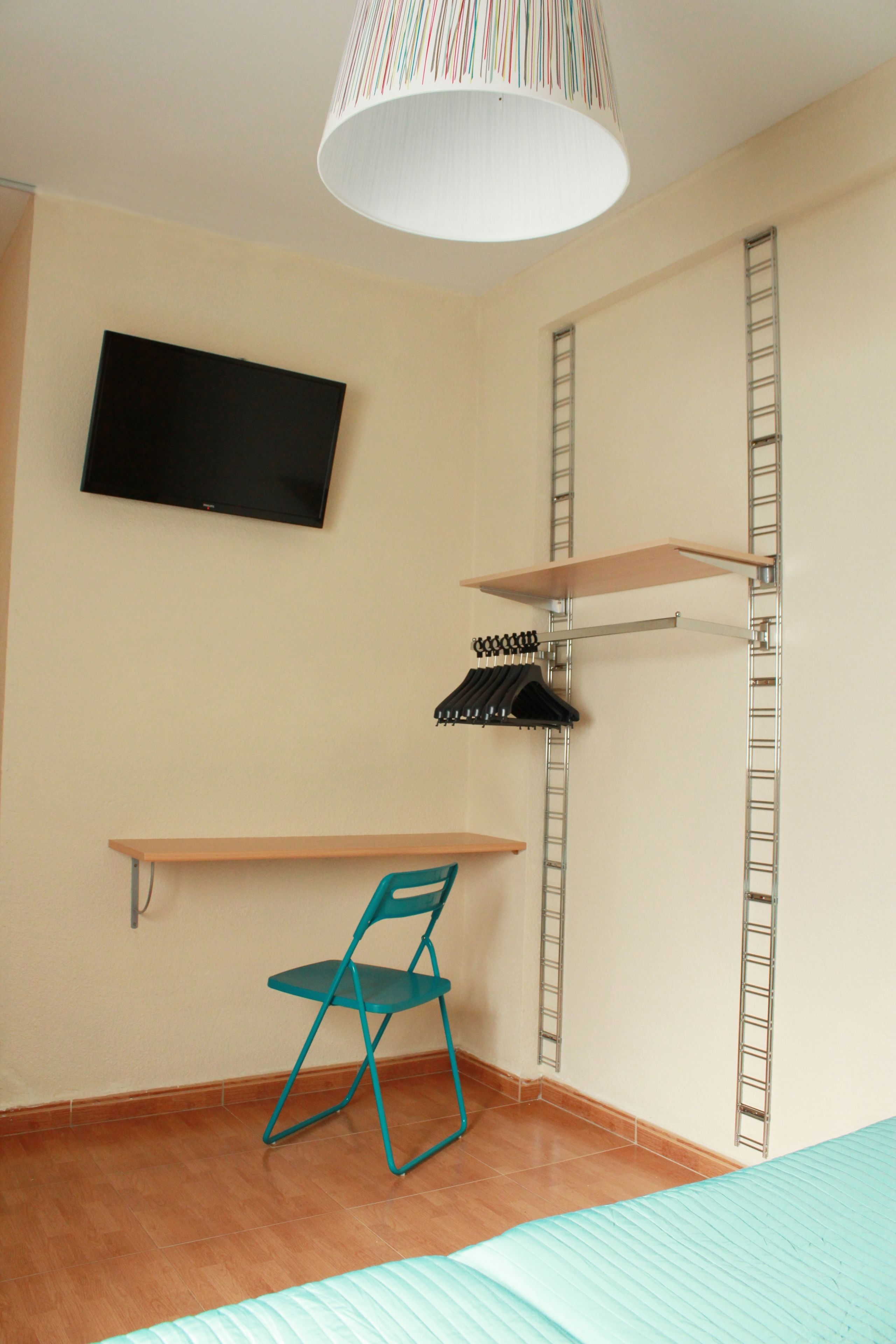 A room with a television mounted on the wall, a chair, shelves, and a hanging rack.