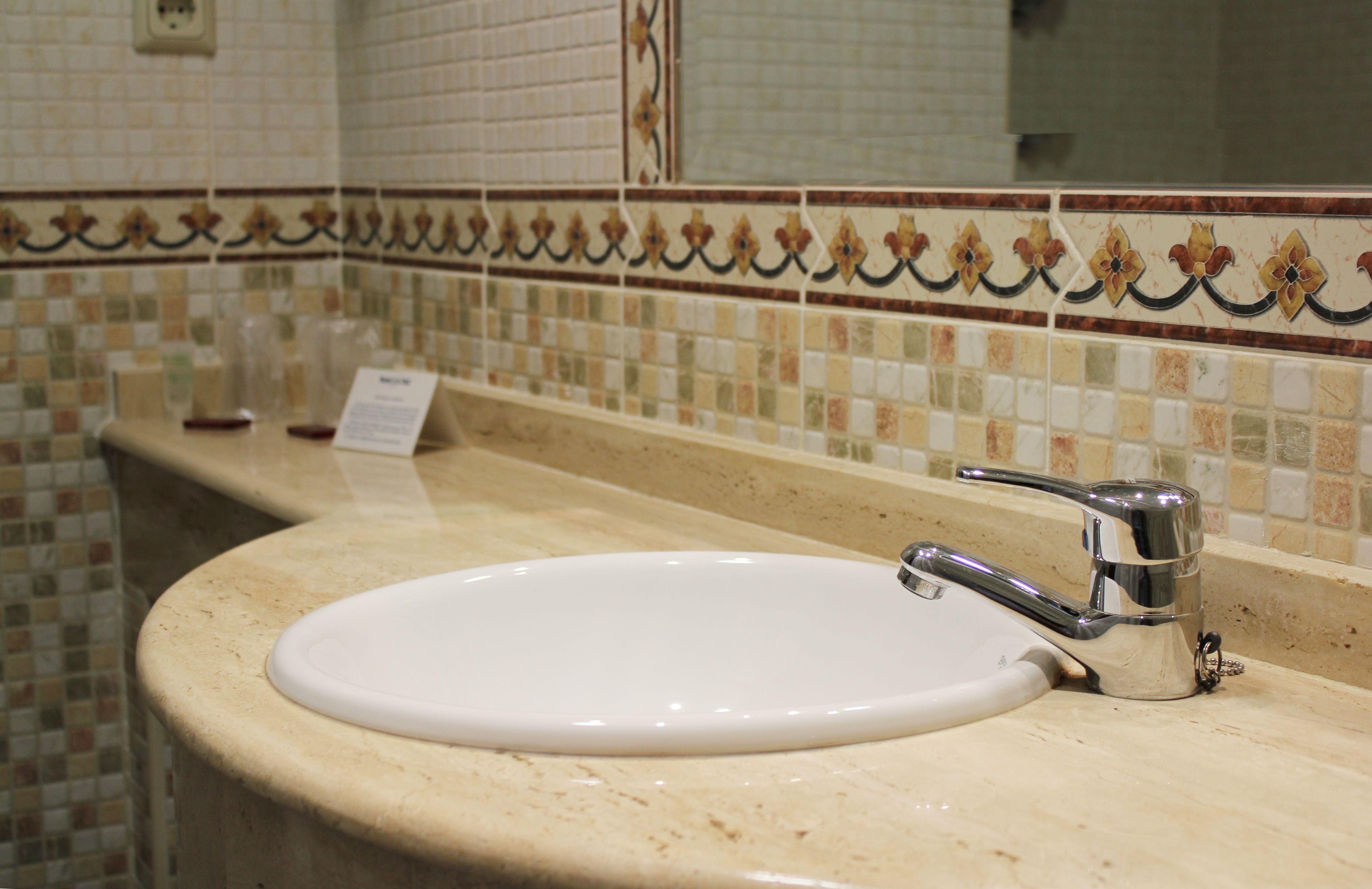 Un lavabo de salle de bain avec un robinet chromé, un miroir au-dessus et un pare-éclaboussures carrelé orné d’un motif floral.