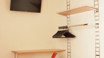 A room with a television mounted on the wall, a red chair, and shelves with hangers.
