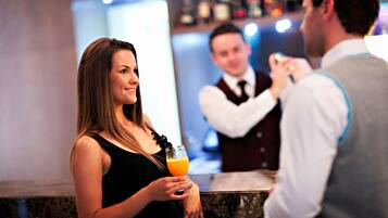 Una mujer sosteniendo una bebida en un bar, con un cantinero al fondo.