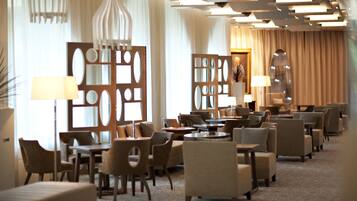 A hotel lobby with multiple seating areas, including sofas and armchairs, arranged around tables. There are decorative panels with cut-out designs and a large mirror on the wall.