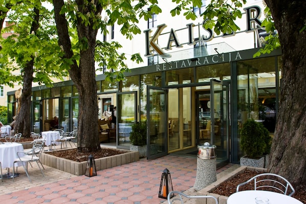 Ein Restaurant mit Außenbereich, großen Bäumen und freiem Blick ins Innere durch Glasüren.