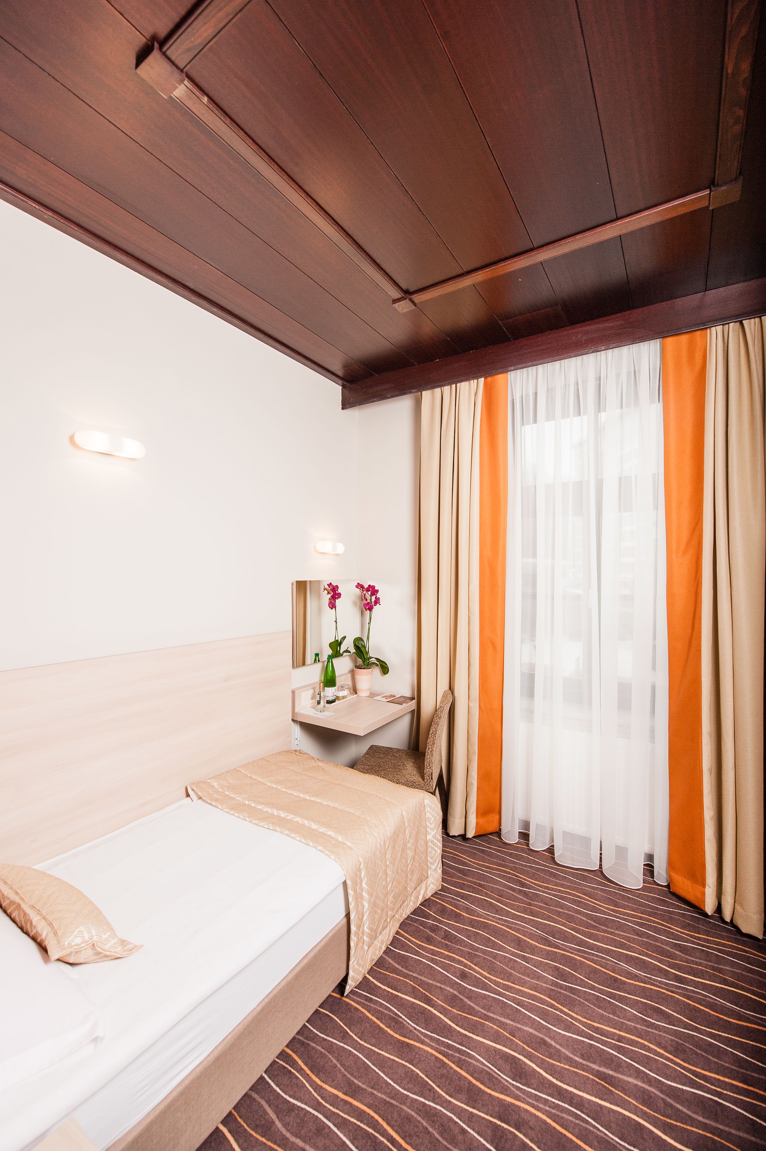Habitación de hotel con cama, una mesita de noche con un florero, un espejo y una ventana con cortinas.