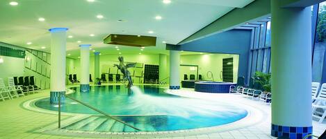 A large indoor swimming pool with a statue in the center, surrounded by lounge chairs and a hot tub.