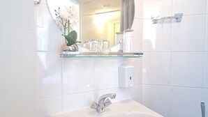 A bathroom with a white sink, a mirror, and a shelf with toiletries. - Hotel 't Witte Huys (The Hague)