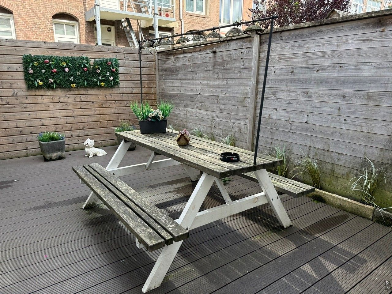 A wooden picnic table with benches, surrounded by a wooden fence and potted plants.