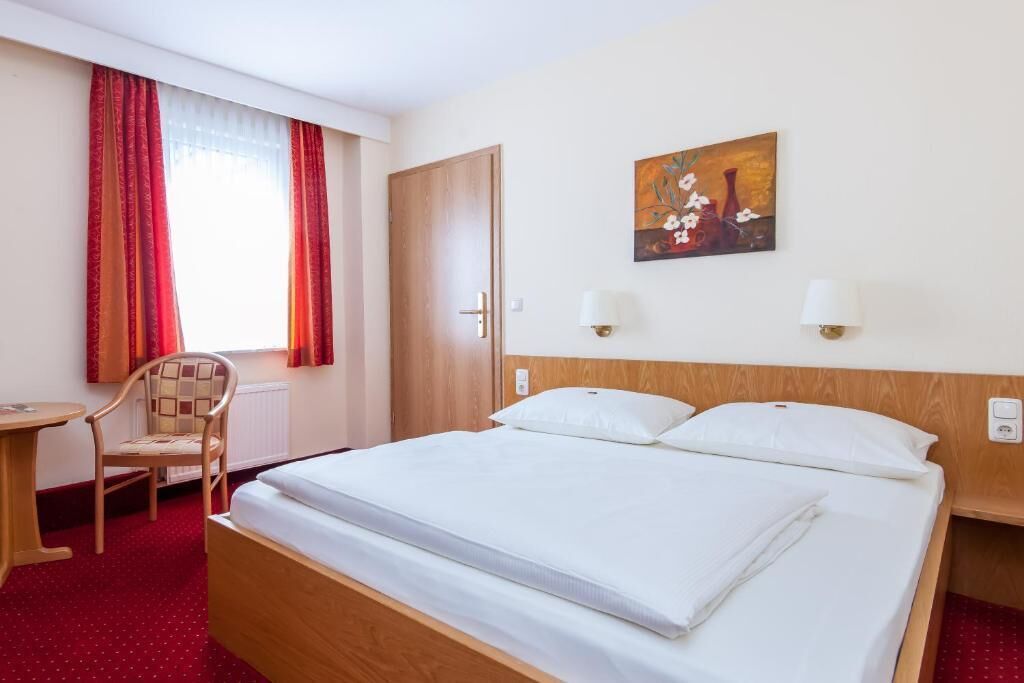 Una habitación de hotel con cama, una silla, un escritorio y un cuadro en la pared.