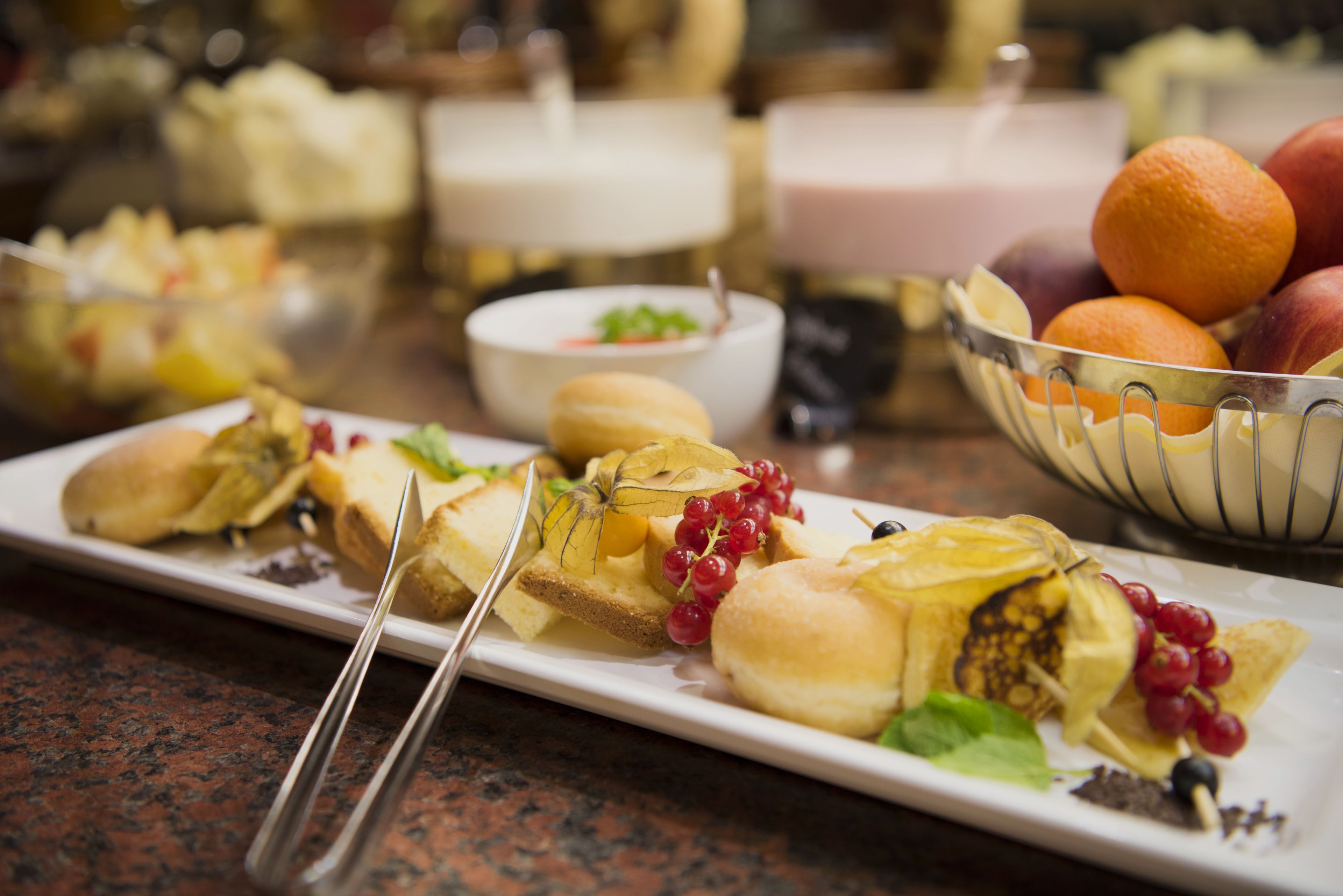 Ein Buffet mit verschiedenen Speisen, darunter ein Teller mit Brot, Obst und einer kleinen Schale roter Trauben.