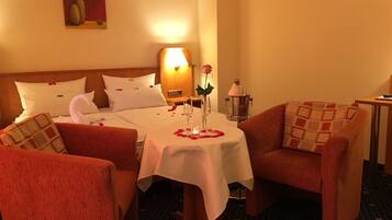 Ein Hotelzimmer mit einem Bett, zwei Sesseln, einem kleinen Tisch mit einer Vase und einer Rose sowie einem Nachttisch mit einer Lampe.
