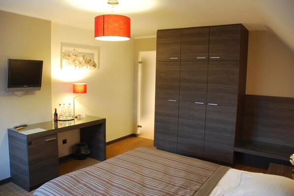 Habitación de hotel con cama, escritorio con lámpara, armario y televisor en la pared.
