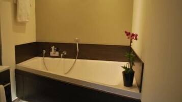 A modern bathroom with a large bathtub, a towel rack, and a potted plant.