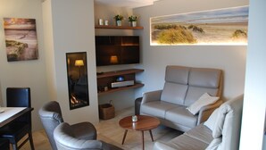 A modern living room with a sofa, chairs, a coffee table, a TV, and artwork on the walls. - Hotel Rubens (De Haan)
