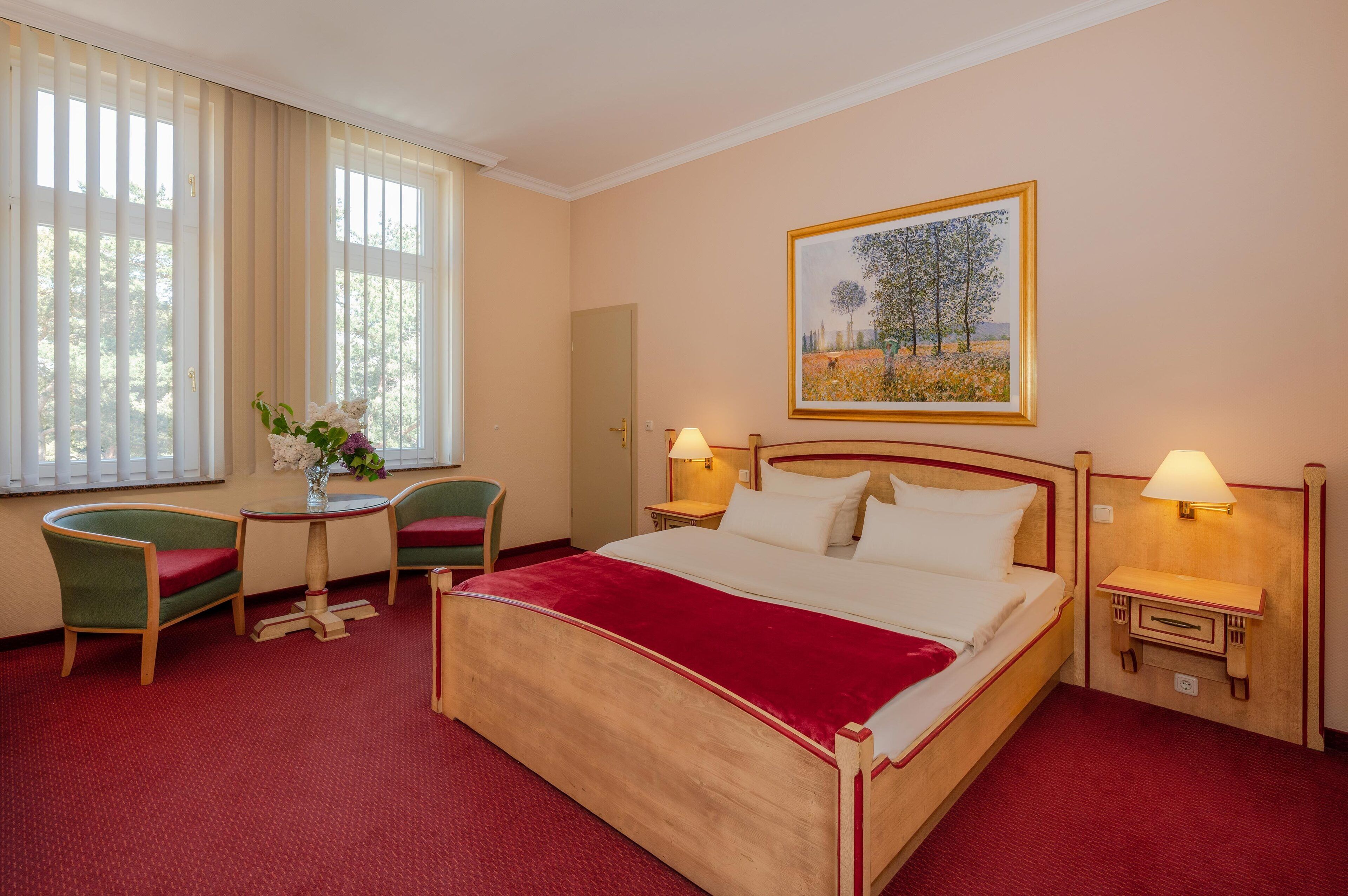 Habitación de hotel con una cama grande, dos sillones, una mesita y un cuadro en la pared.