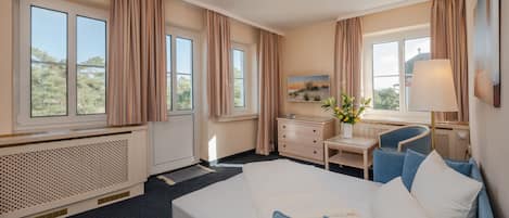 A hotel room with a large bed, a desk with a chair, a dresser, and a window with curtains.