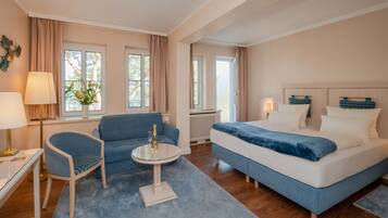 A hotel room with a bed, a sofa, a small table with a bottle, and a lamp.