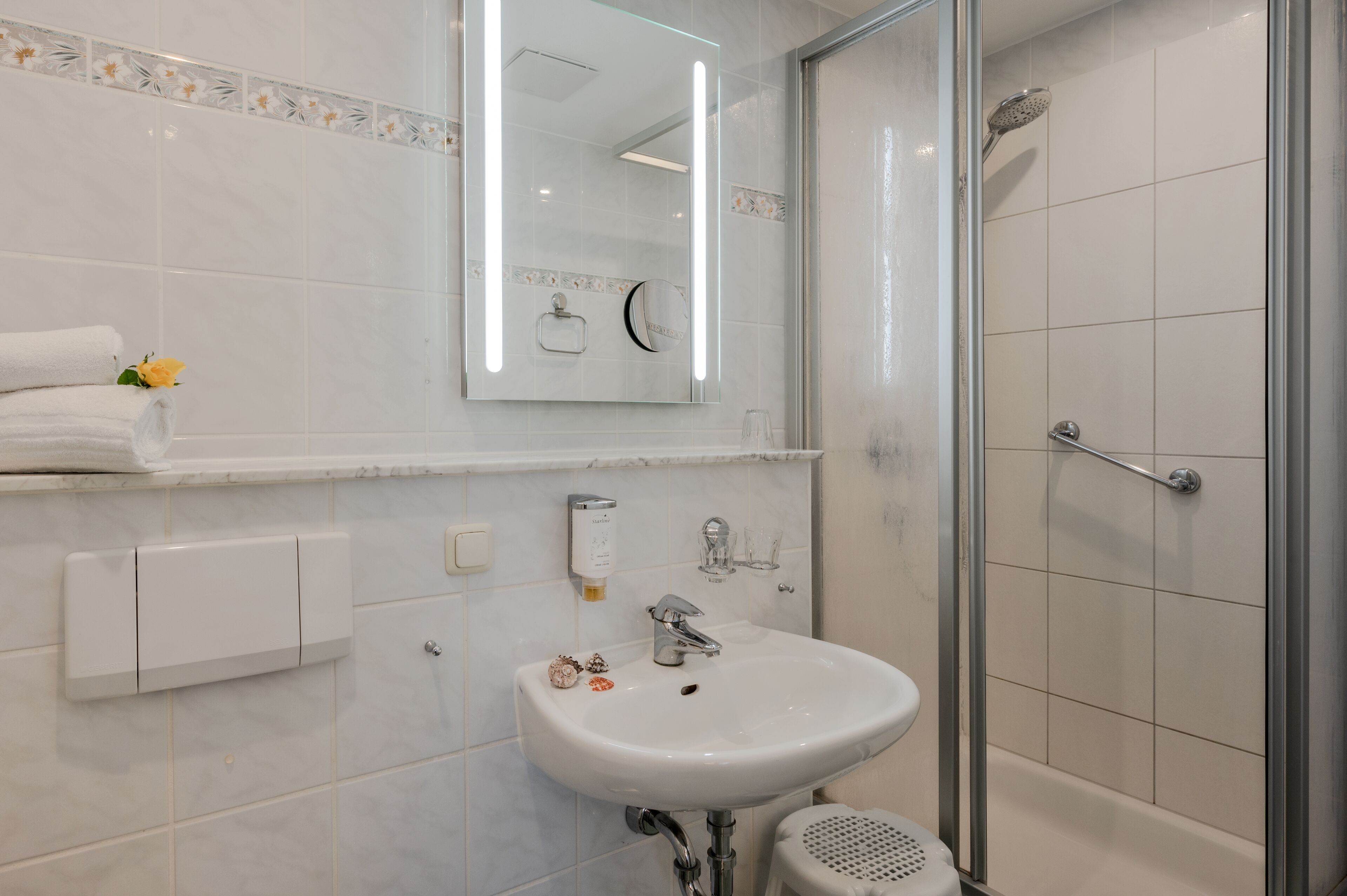 Un bagno moderno con lavandino bianco, specchio e cabina doccia in vetro.
