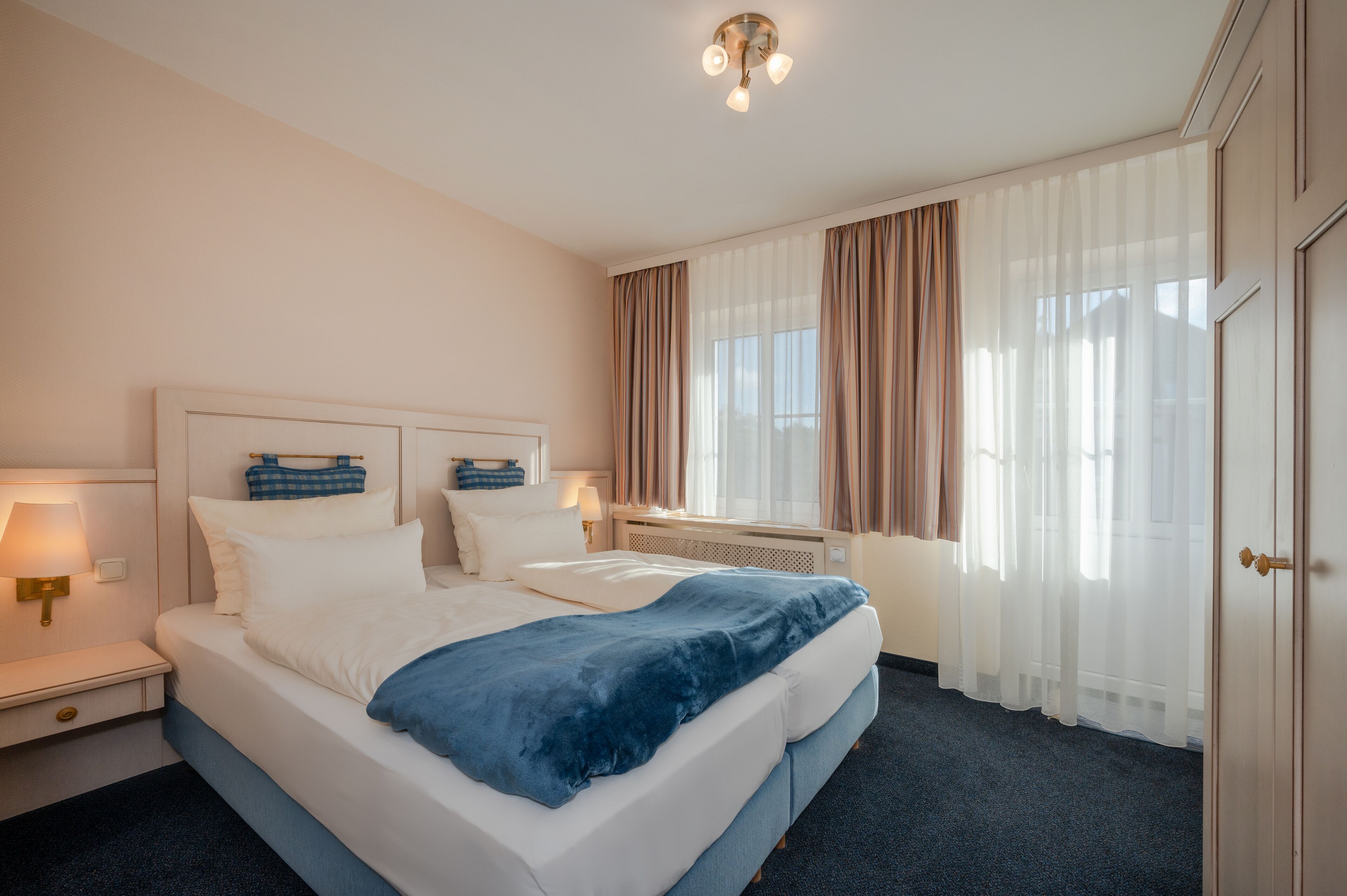 Habitació d'hotel amb un llit gran, làmpades de nit, una finestra amb cortines i una porta.