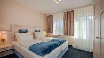 Habitació d'hotel amb un llit gran, làmpades de nit, una finestra amb cortines i una porta.