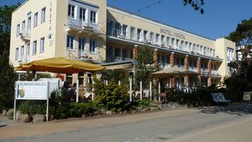 A hotel with a yellow facade, multiple balconies, outdoor seating, and a sign indicating a restaurant.