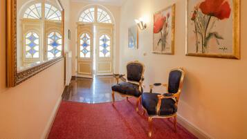 A hallway with two ornate chairs, a red carpet, and a large mirror.