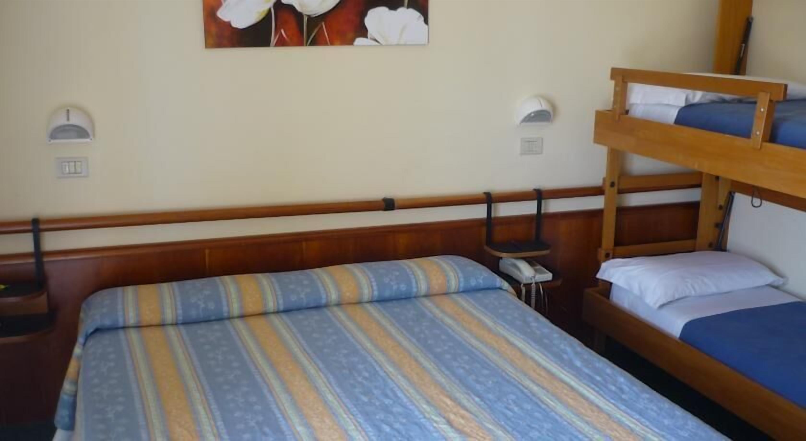 Une chambre avec un lit superposé, une couette à rayures, un téléphone sur la table de chevet et des lampes fixées au mur.